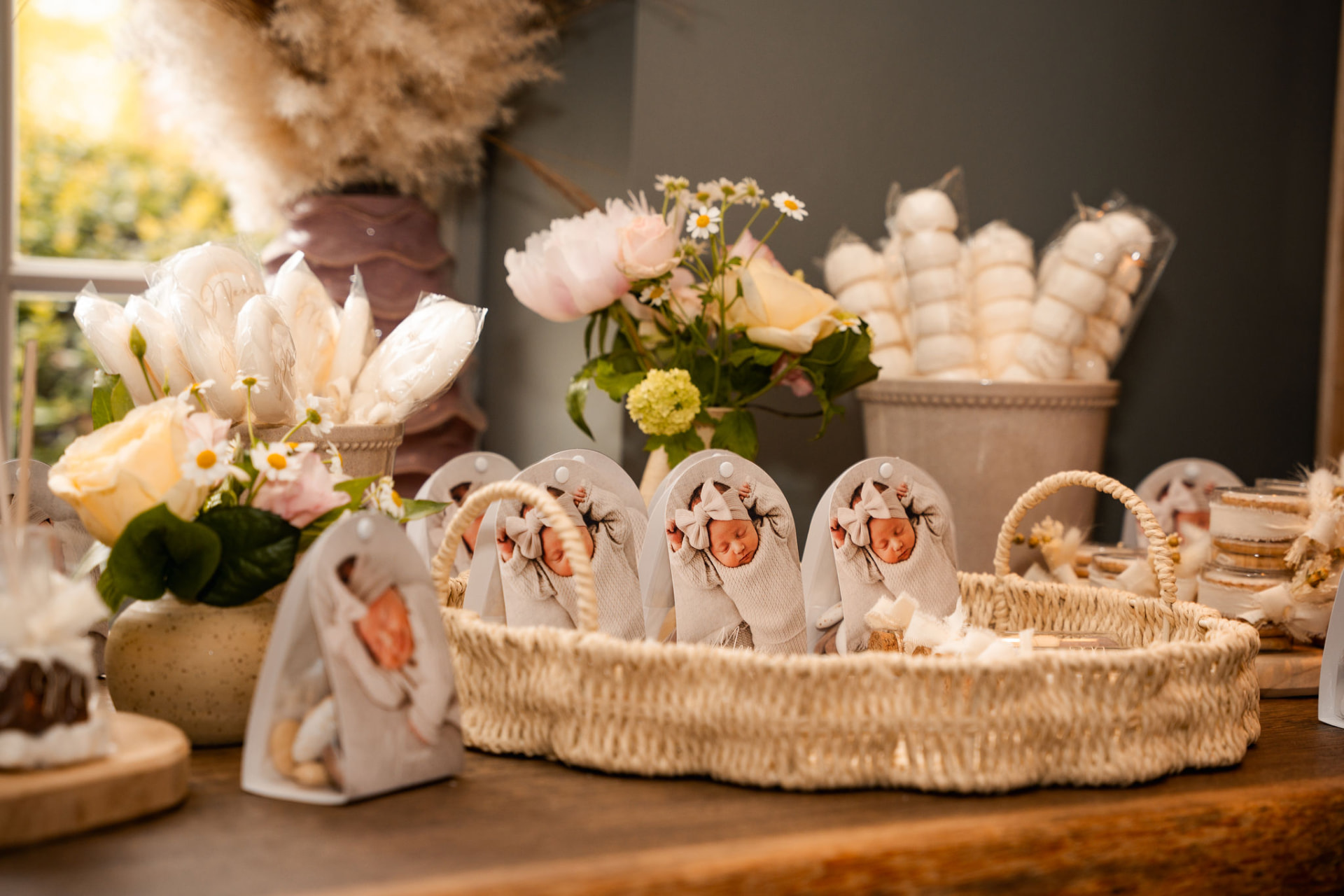 Bedankjes met babyfoto in een mand naast bloemen en marshmallows