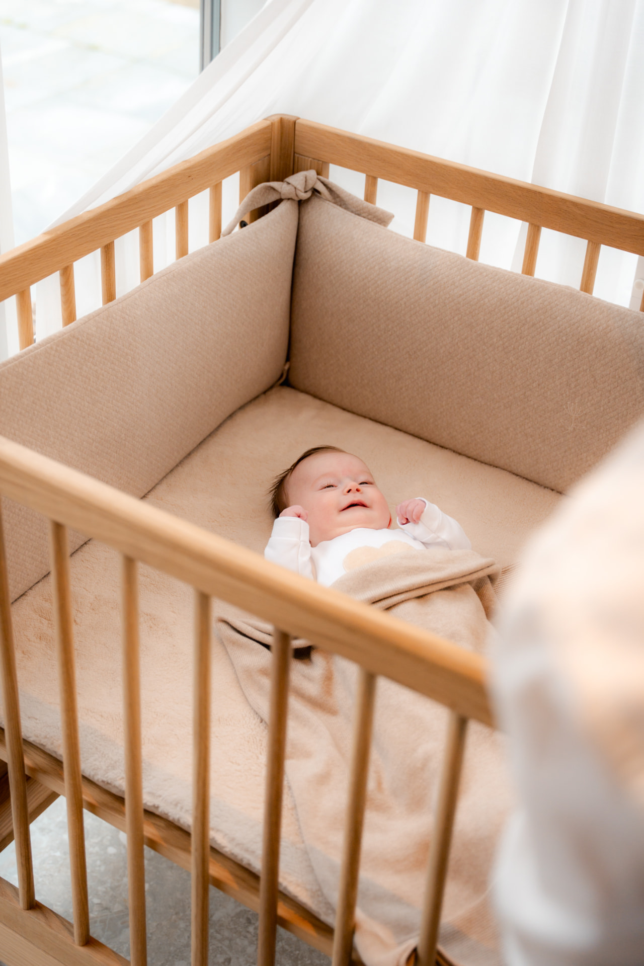 Baby ligt lachend in een houten babybed