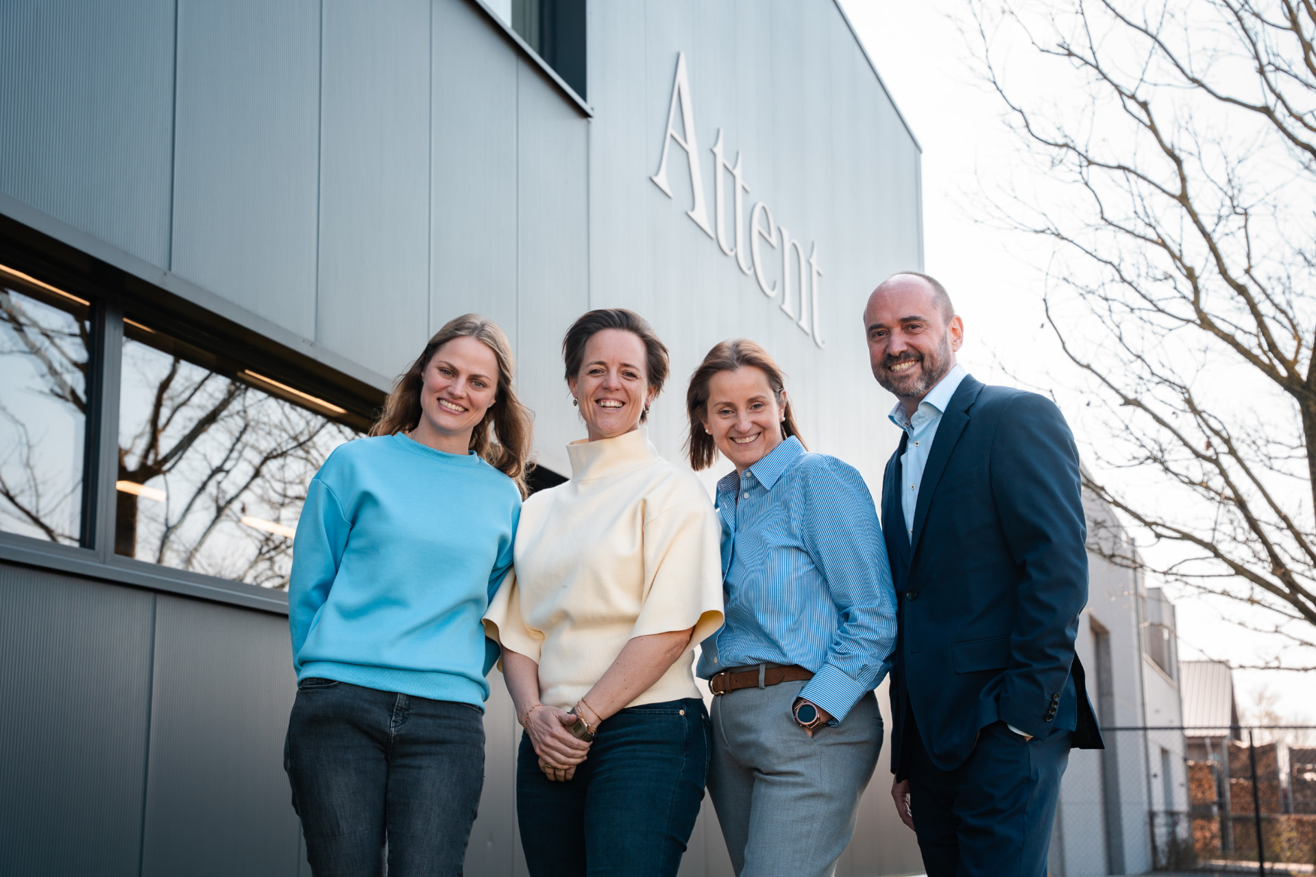 Het team van Attent lachend voor het bedrijfsgebouw met de naam Attent op de gevel