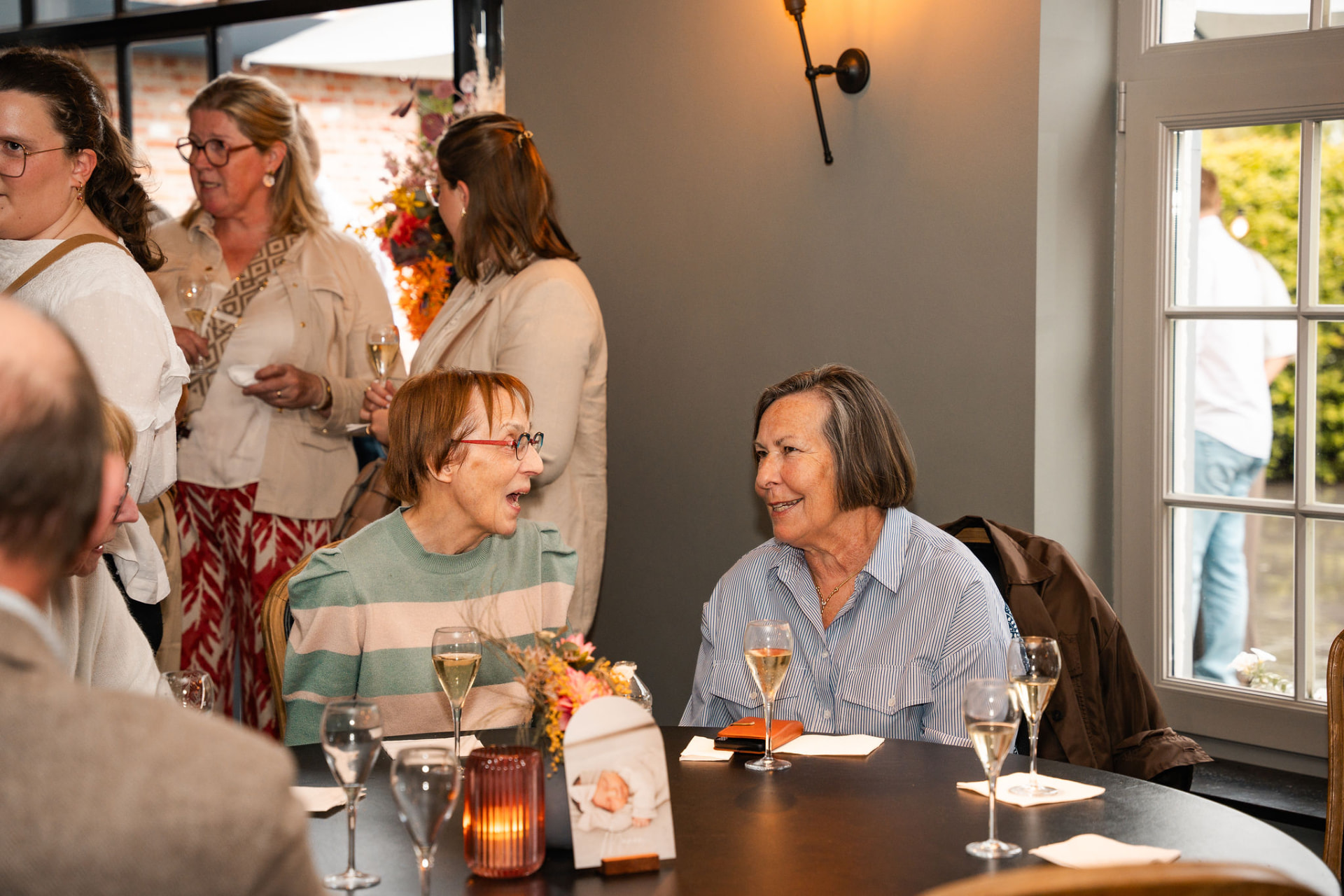 Twee gasten lachend in gesprek aan tafel met een glas cava