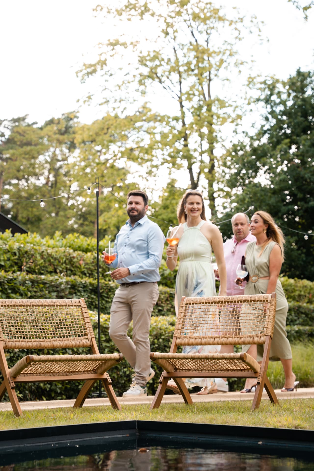 Gasten met aperitief wandelen langs de rieten stoelen bij het water
