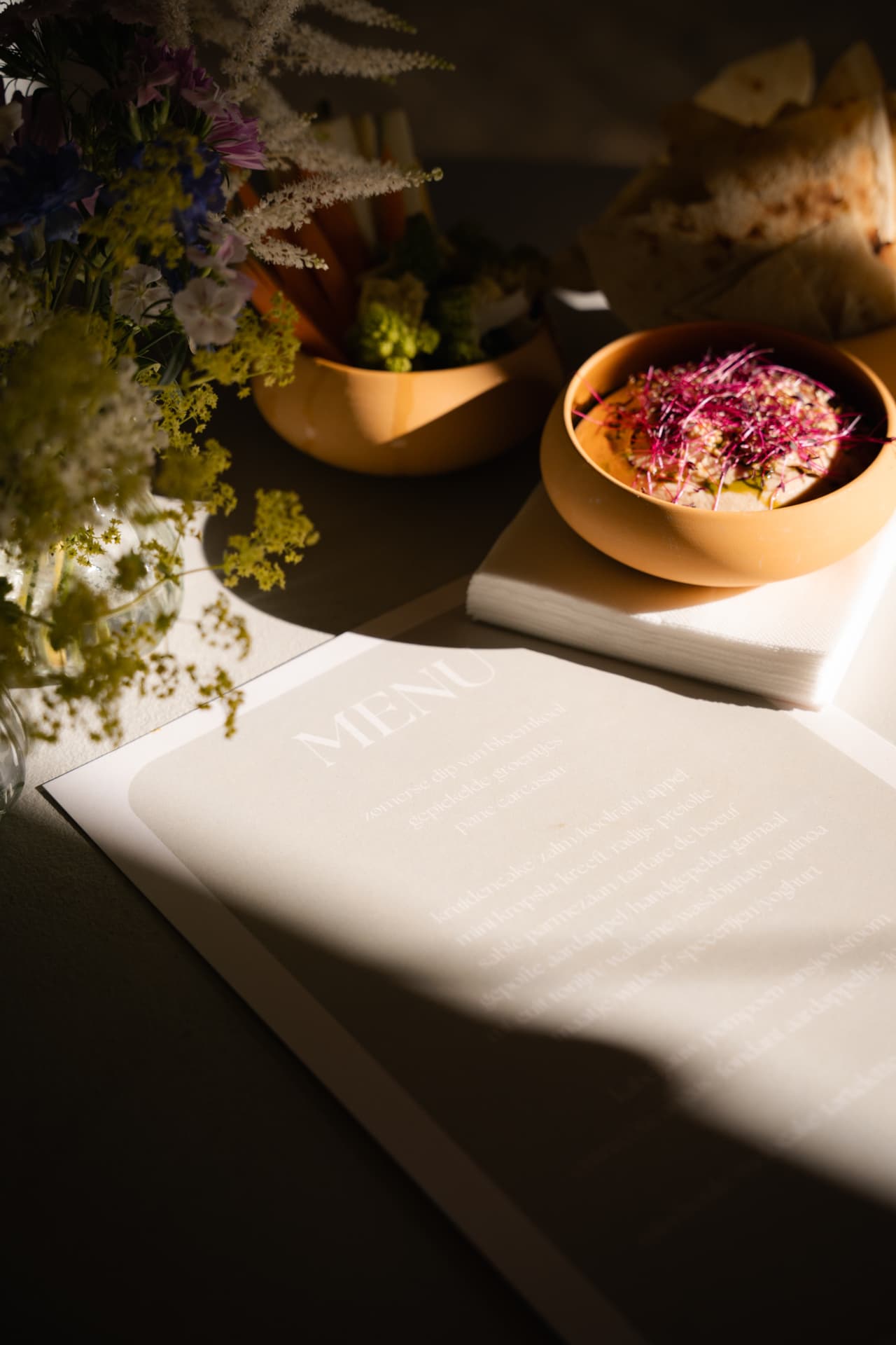 Menukaart met hapjes en bloemen in strijklicht