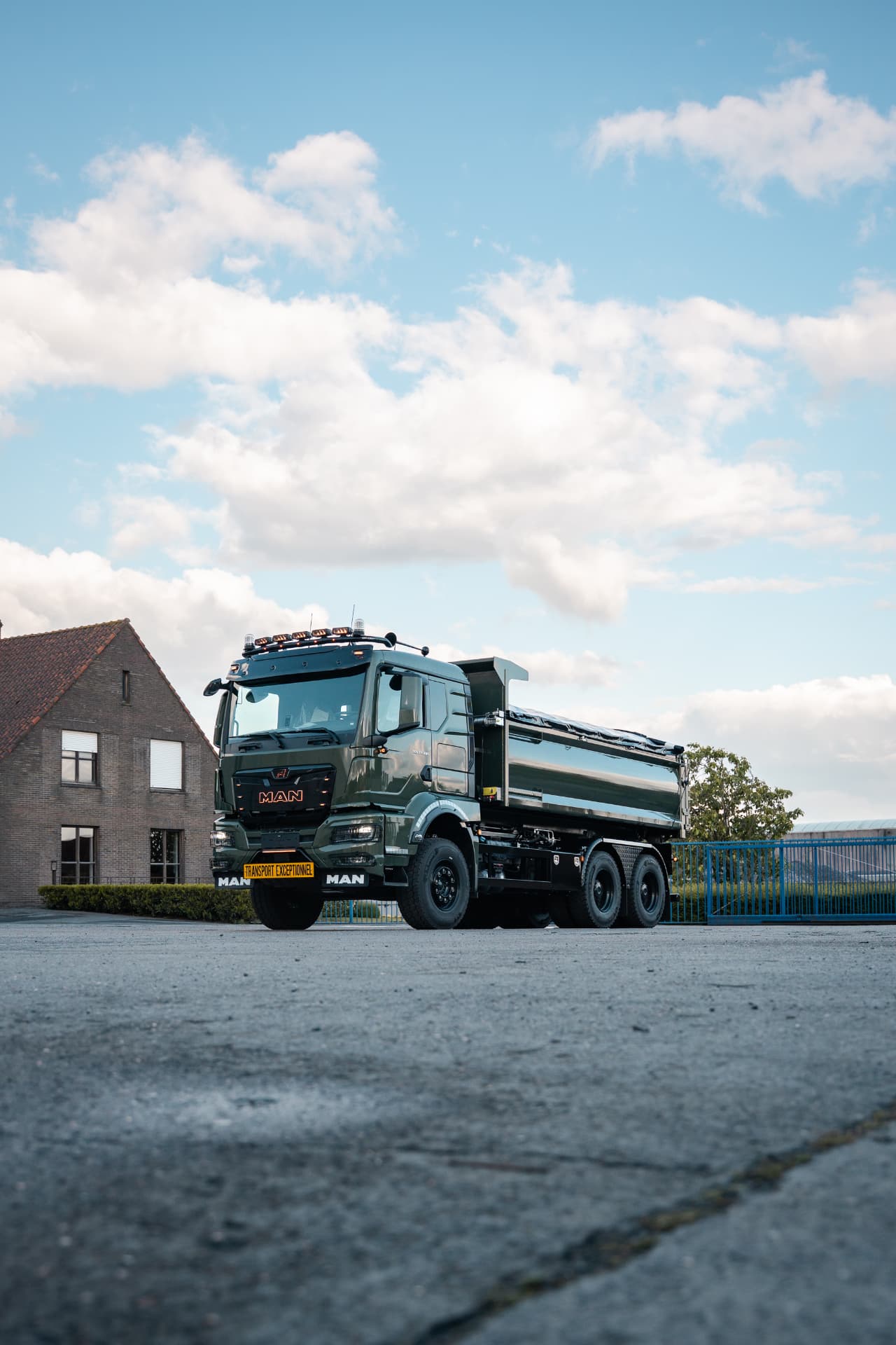 Groene MAN-kipper met inox bak op een erf bij avondlicht