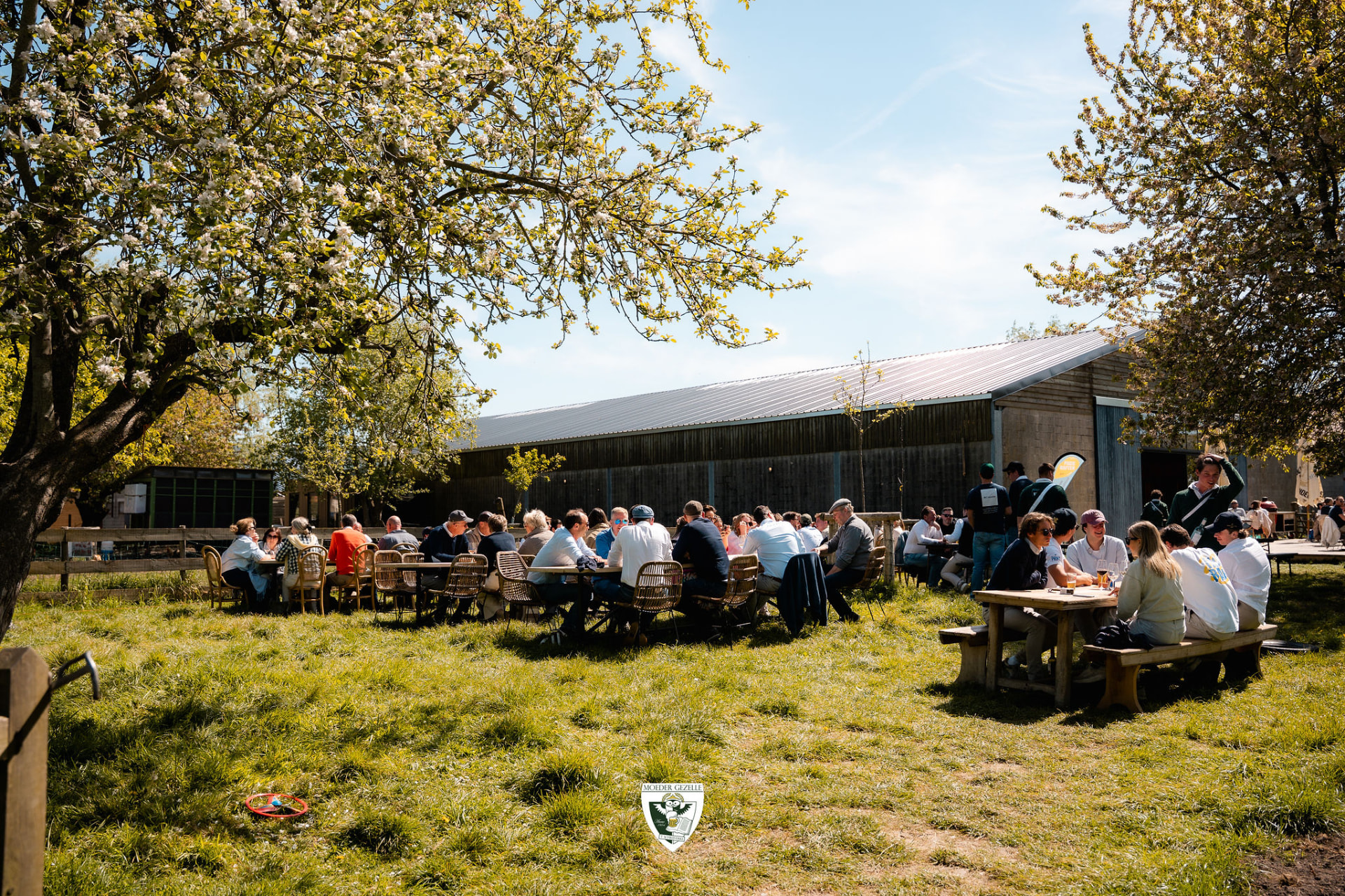 Deelnemers aan tafel in de zon voor de hoeve tussen bloesembomen