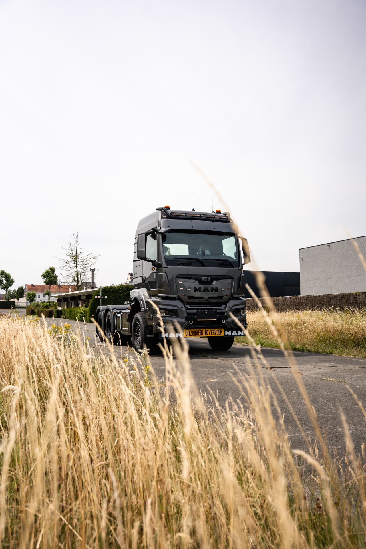 Grijze MAN-trekker op een landweg geflankeerd door hoog gras