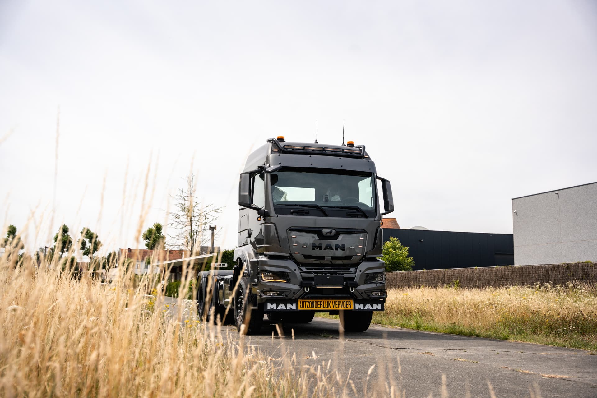 Grijze MAN-trekker met bord uitzonderlijk vervoer langs een landweg