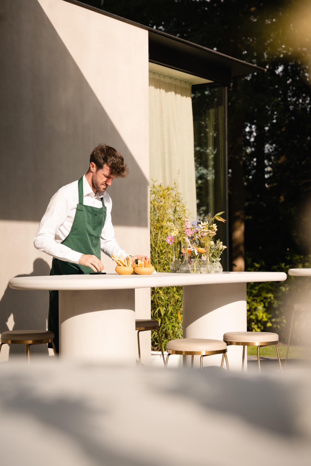 Medewerker in groene schort maakt hapjes klaar aan de buitentafel