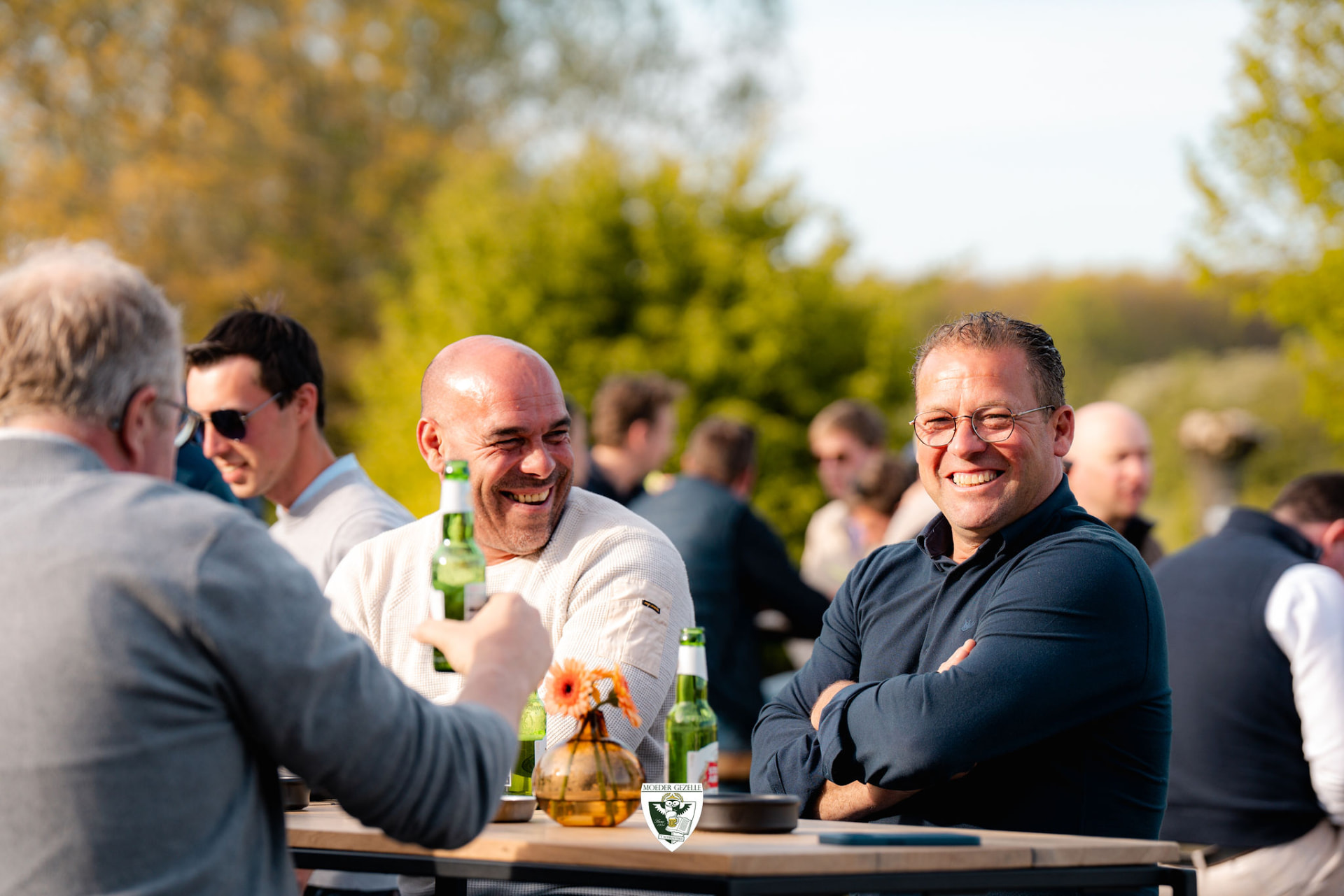 Lachende gasten met een biertje aan een tafel in de avondzon