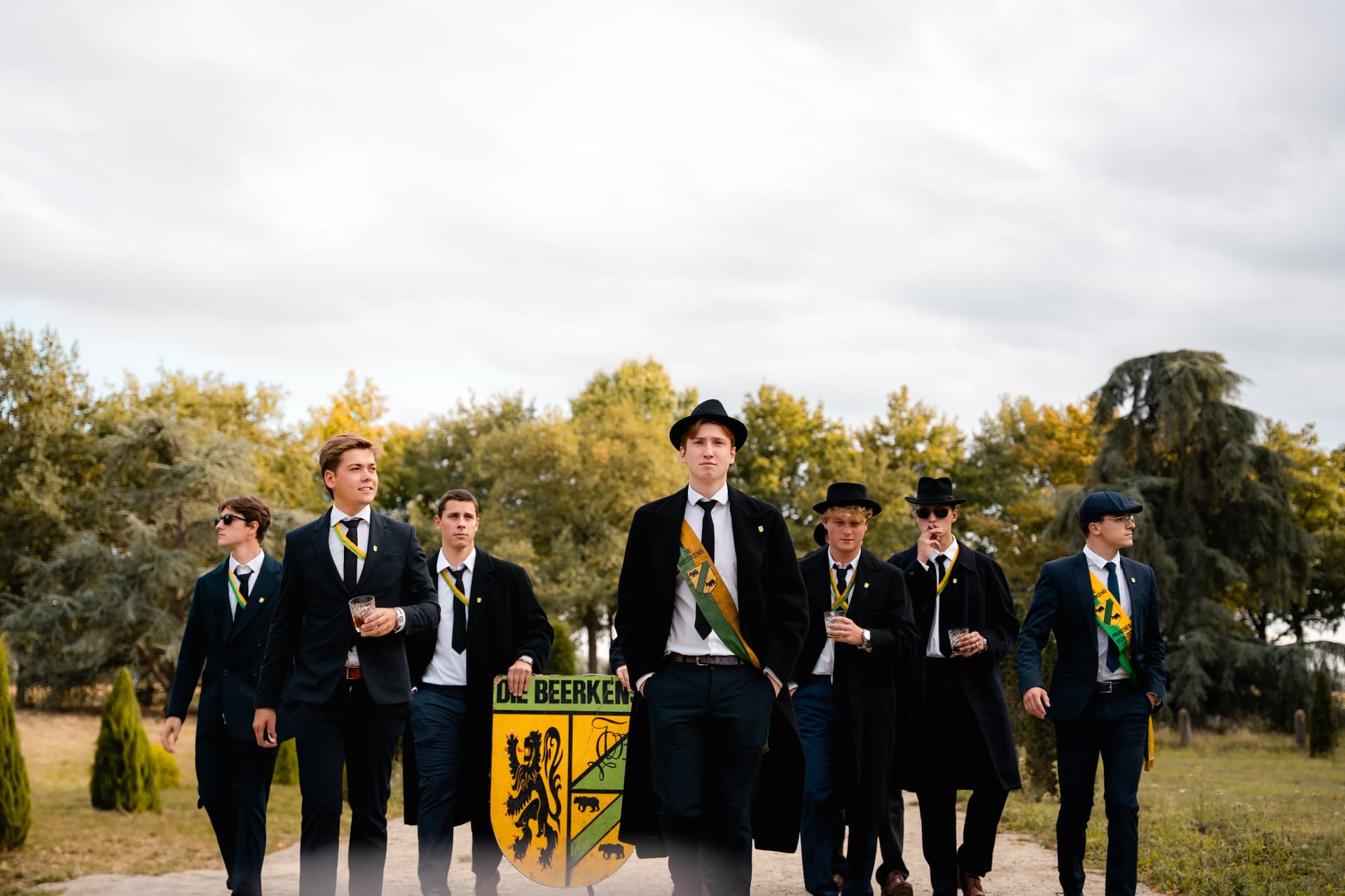 Leden van Studentenclub Die Beerkens wandelen met hun schild over een dreef
