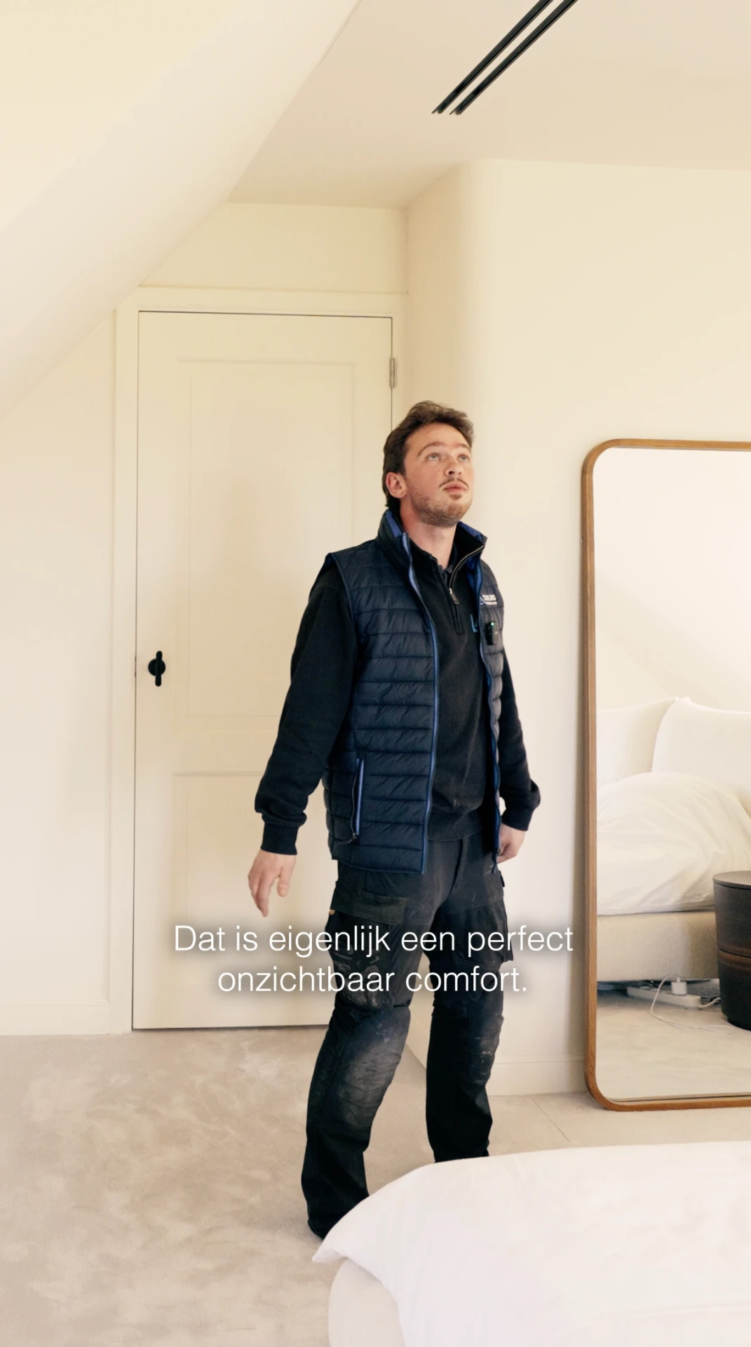 Technicus in een lichte slaapkamer kijkt naar een onzichtbare airco-unit aan het plafond
