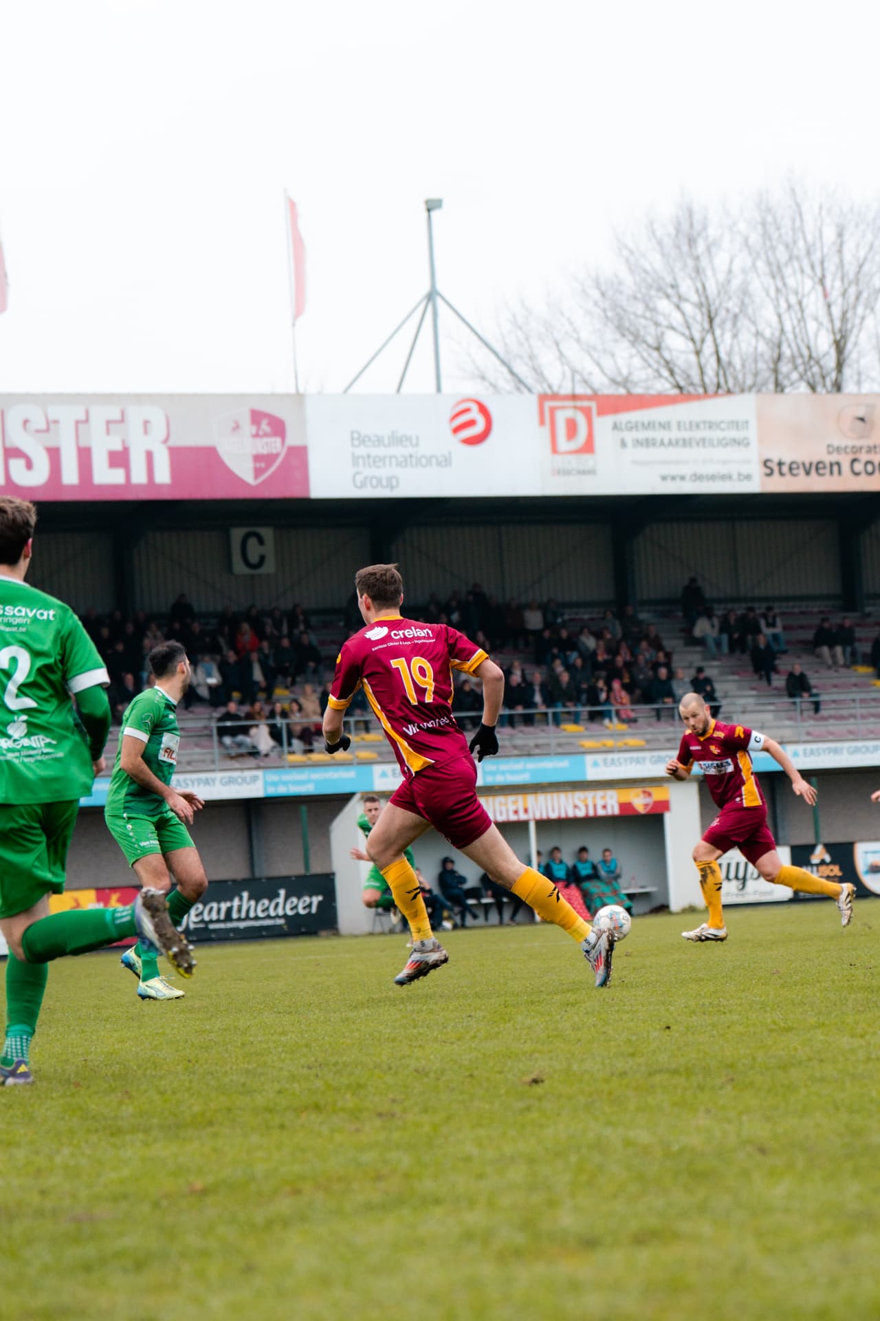 Speler met rugnummer 19 in duel met de tegenstander voor de tribune
