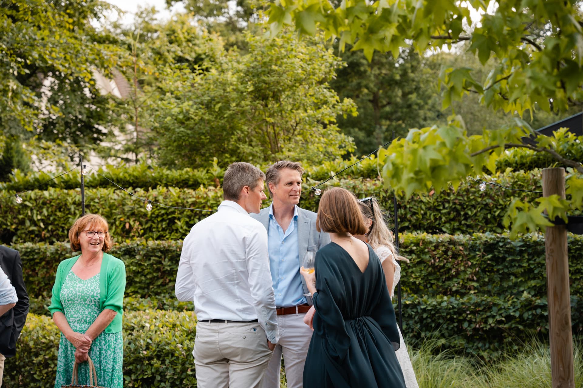 Gasten in gesprek met een glas wijn onder de lichtslingers