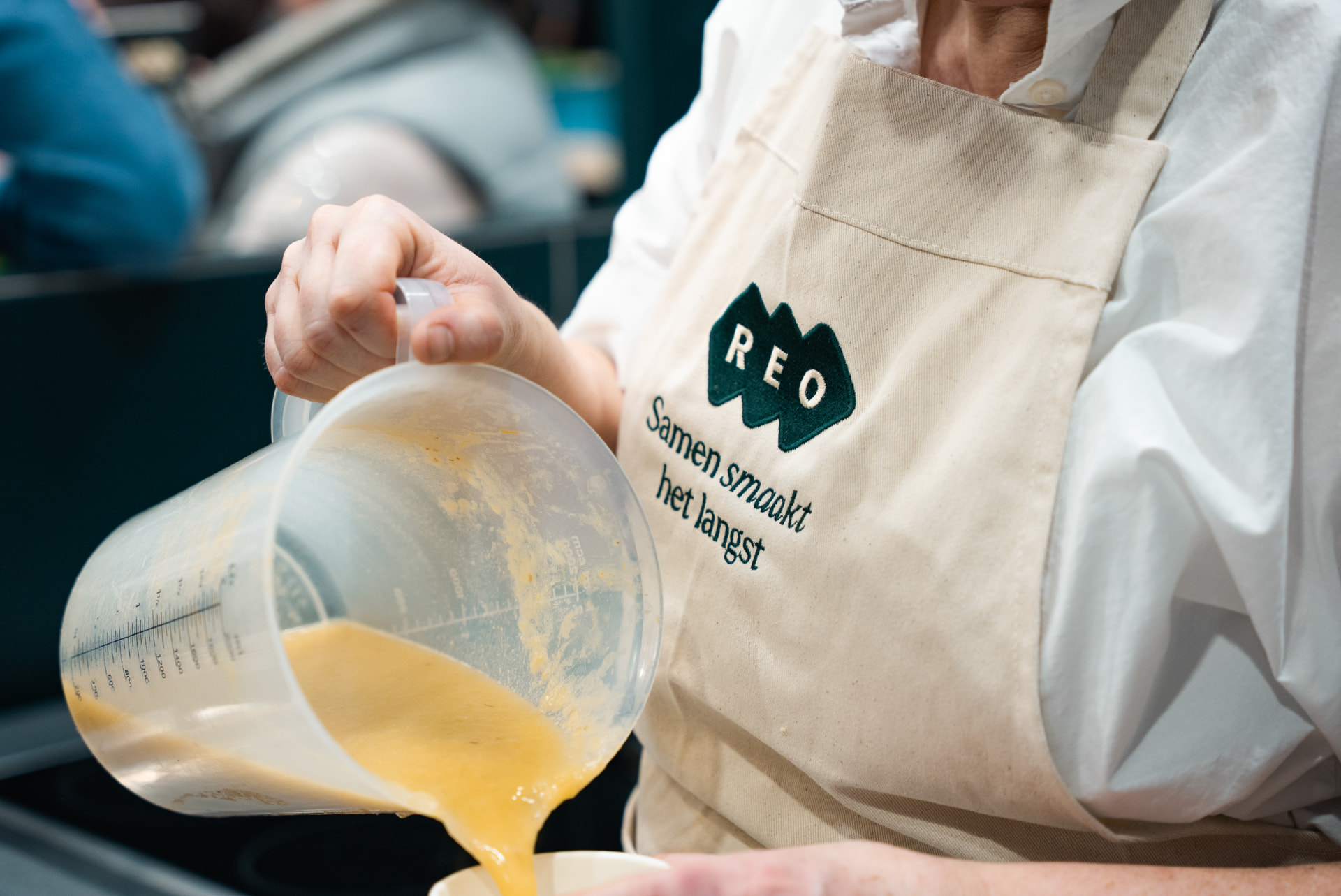 Medewerker in REO-schort giet verse soep uit een maatbeker tijdens een REO-event