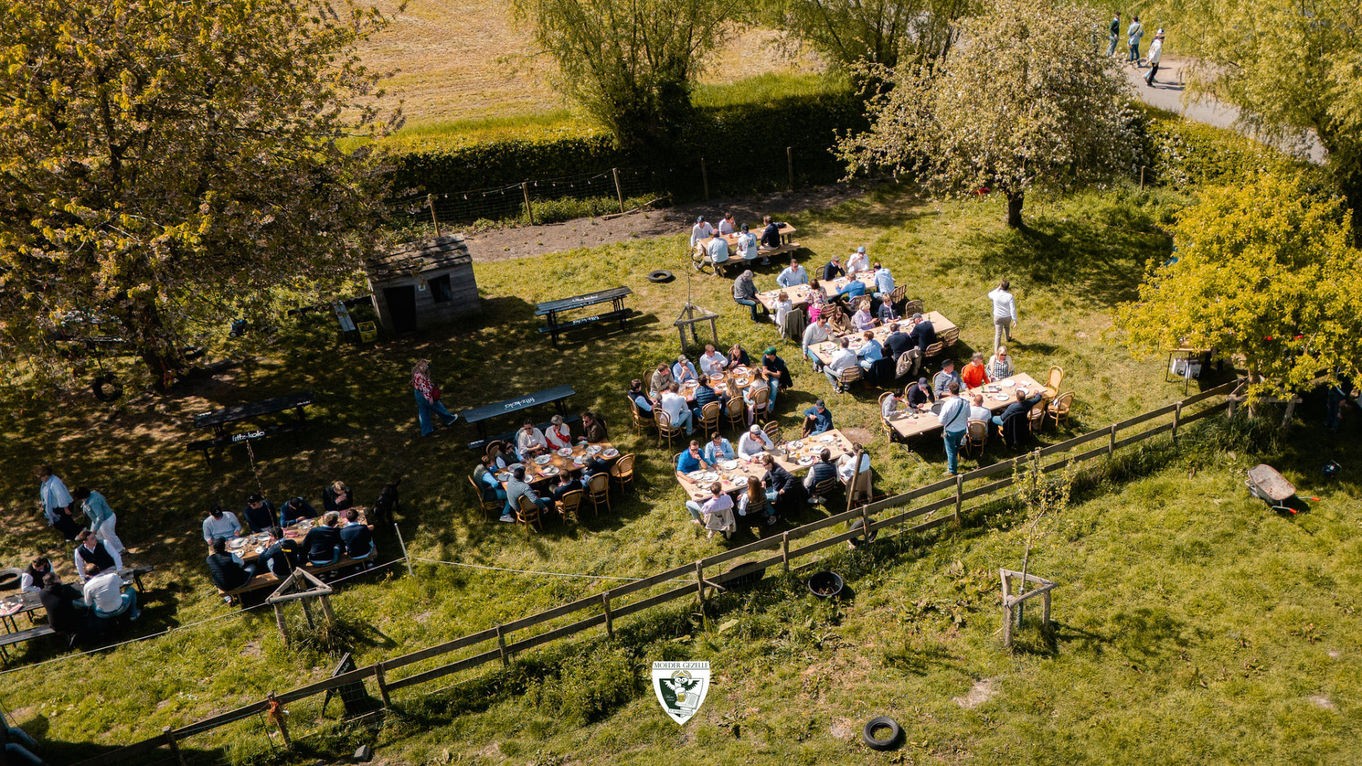 Luchtbeeld van de deelnemers aan lange tafels in de boomgaard